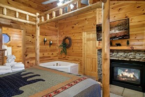 Interno di una baita di legno con camino in pietra, una vasca da bagno e una grande finestra.