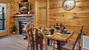 A wooden cabin interior with a stone fireplace, dining table set with dishes, and a television mounted above the fireplace. - Spacious Cozy Cabin - Best of Both Worlds (Gatlinburg)