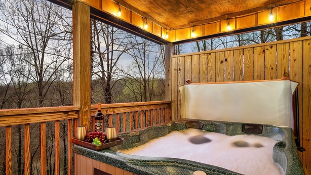 A wooden deck with a hot tub, wooden railings, and a view of trees. - Spacious Cozy Cabin - Best of Both Worlds (Gatlinburg)