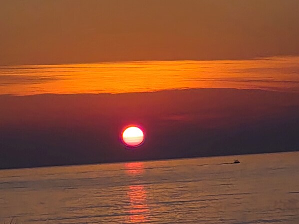 A sunset over a calm body of water with a boat in the distance. - Self-contained 75 m2 apartment on the ground floor of a villa, air-conditioned, seafront (L'Île-Rousse)