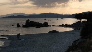 A beach with boats, rocky outcrops, and a person walking. - Self-contained 75 m2 apartment on the ground floor of a villa, air-conditioned, seafront (L'Île-Rousse)