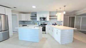 Une cuisine moderne avec des meubles blancs, un îlot central, des appareils en acier inoxydable et des luminaires suspendus.