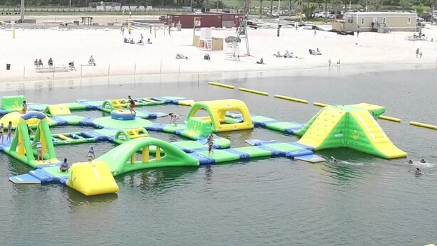 Un espace de jeux aquatiques en plein air, avec des structures gonflables et une plage de sable en arrière-plan.