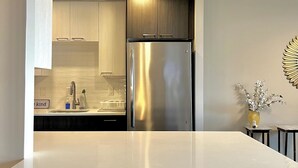 Eine moderne Küche mit Edelstahl-Kühlschrank, weißen Schränken und einer zentralen Kochinsel mit Sitzgelegenheiten.