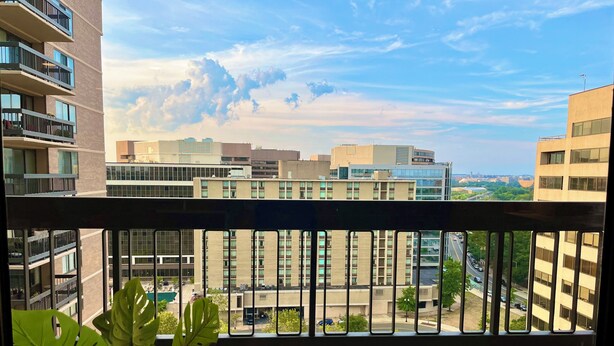 Ein Balkon mit Blick auf eine Stadtansicht, darunter moderne Gebäude und ein klarer Himmel.
