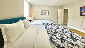 Ein Hotelzimmer mit zwei Betten, einem an der Wand befestigten Fernseher und einer Tür zu einem weiteren Raum.