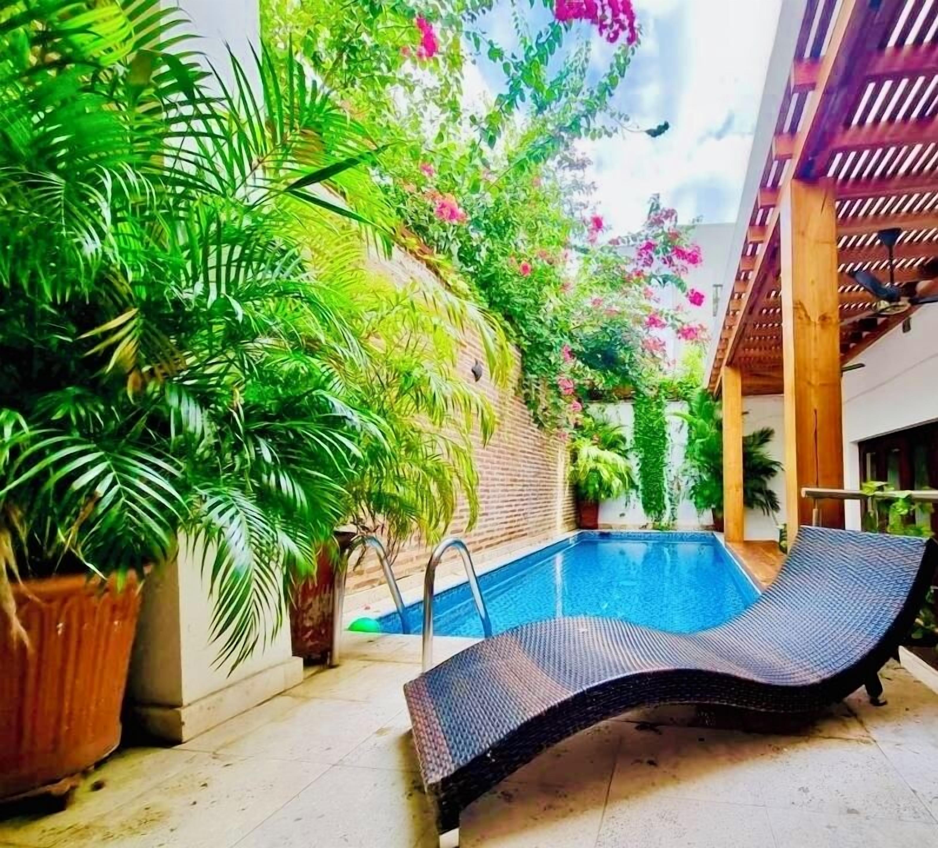 Une piscine intérieure avec des chaises longues, entourée d’une végétation luxuriante et agrémentée d’une pergola en bois.