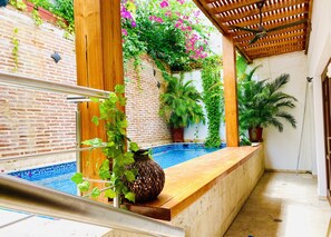 Un espacio al aire libre techado con piscina, vigas de madera y plantas en macetas.