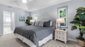 A bedroom with a bed, nightstands, a ceiling fan, a window with blinds, and a potted plant.