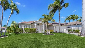 A residential house with a well-maintained lawn, palm trees, and a clear blue sky.