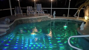 A swimming pool with blue lighting effects, surrounded by lounge chairs and a covered area with steps leading into the pool.