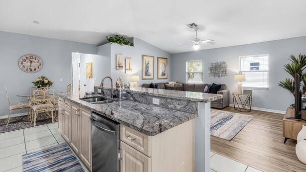 A modern kitchen with granite countertops, a dishwasher, and a dining area with a table and chairs.