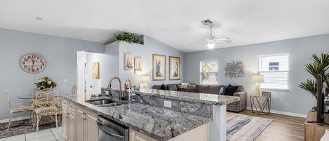 A modern kitchen with granite countertops, a dishwasher, and a dining area with a table and chairs.