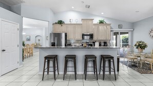 A modern kitchen with light wood cabinets, stainless steel appliances, and a central island with bar stools.