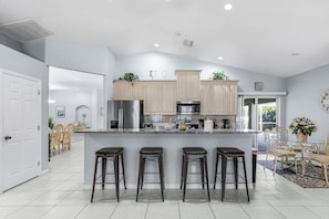 Una cocina moderna con armarios de madera clara, electrodomésticos de acero inoxidable y una isla central con taburetes de bar.