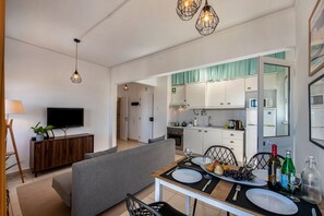 A modern kitchen with white cabinets, a dining table set for two, and a TV in the living area. - Apartment in the city center! (Faro)