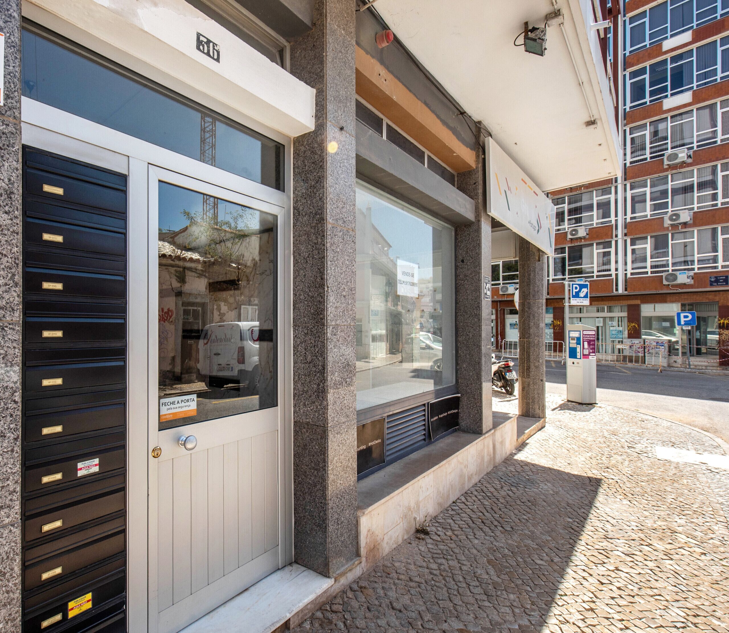 A building with a large glass window, a door with a sign, and a parking sign on the sidewalk.