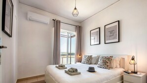 Ett hotellrum med en säng, sängbord, ett litet bord, en lampa, en fotoram, en luftkonditioneringsanläggning och utsikt över omgivningen.
