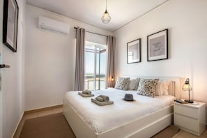 Una camera d'albergo con un letto, comodini, una lampada, una cornice e un climatizzatore, oltre a vista sull'esterno.