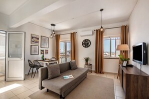 A modern living room with a sofa, dining table, chairs, a TV, and a window with curtains. - Apartment in the city center! (Faro)