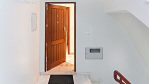 A hallway with a wooden door, a doormat, a light switch, and a mailbox.