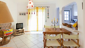 A dining area with a wooden table, chairs, a television, and a wicker chair with a colorful cushion.