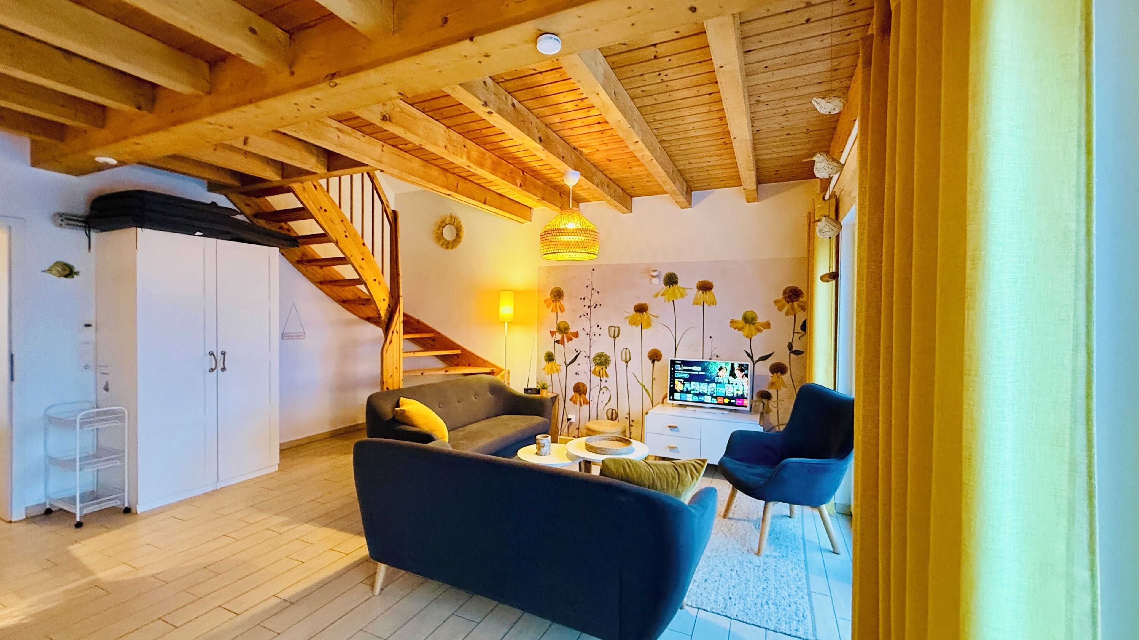 Ein gemütliches Wohnzimmer mit einer Couch, einem blauen Sessel, einem kleinen Tisch, einem Fernseher und einer Treppe.