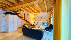 A cozy living room with a sofa, a blue armchair, a small table, a TV, and a staircase.