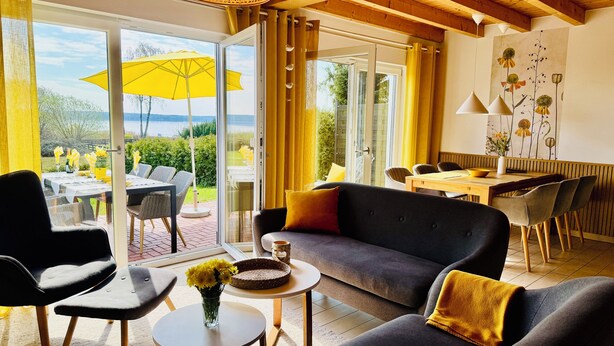 A modern living room with a sofa, chairs, a dining table, and a view of the outdoors.