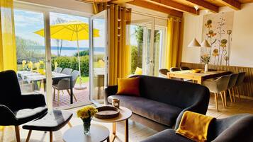 Ein modernes Wohnzimmer mit einer Couch, Sesseln, einem Esstisch und Blick ins Freie.