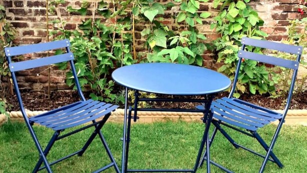 A blue metal table and chairs set in a garden with a brick wall and green plants in the background. - Entire House in Canterbury Centre - Free Parking - WiFi (Canterbury)