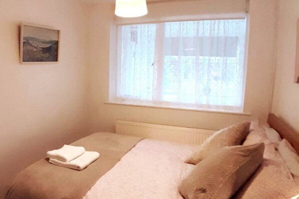 Een slaapkamer met een bed, een raam met gordijnen, een radiator en een schilderij aan de muur.