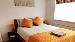 A neatly made bed with a white and yellow quilt, two orange pillows, and a folded towel on the bed. - Entire House in Canterbury Centre - Free Parking - WiFi (Canterbury)