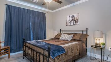 Un dormitorio con una cama, un ventilador de techo, una mesita de noche, una lámpara y un cuadro en la pared.