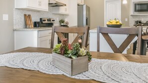 Une cuisine avec des meubles blancs, une table à manger en bois et un set de table en fibres tressées.