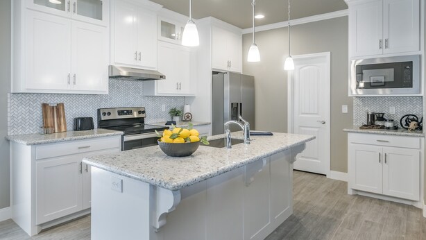 Une cuisine moderne avec des meubles blancs, des plans de travail en granit, des appareils électroménagers en acier inoxydable et des luminaires suspendus.
