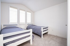 A bedroom with two single beds, a window with blinds, and a carpeted floor.