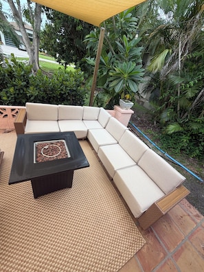 An outdoor seating area with a sofa and a table, surrounded by greenery and a yellow canopy. - Walk to Beach 2- Patios Updated Lux Retreat NEW Heated Pool Sleeps 10 Small Dogs (Naples)