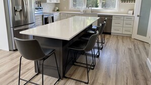 Een moderne keuken met een centraal kookeiland, roestvrijstalen apparatuur en een groot raam met uitzicht op de omgeving.