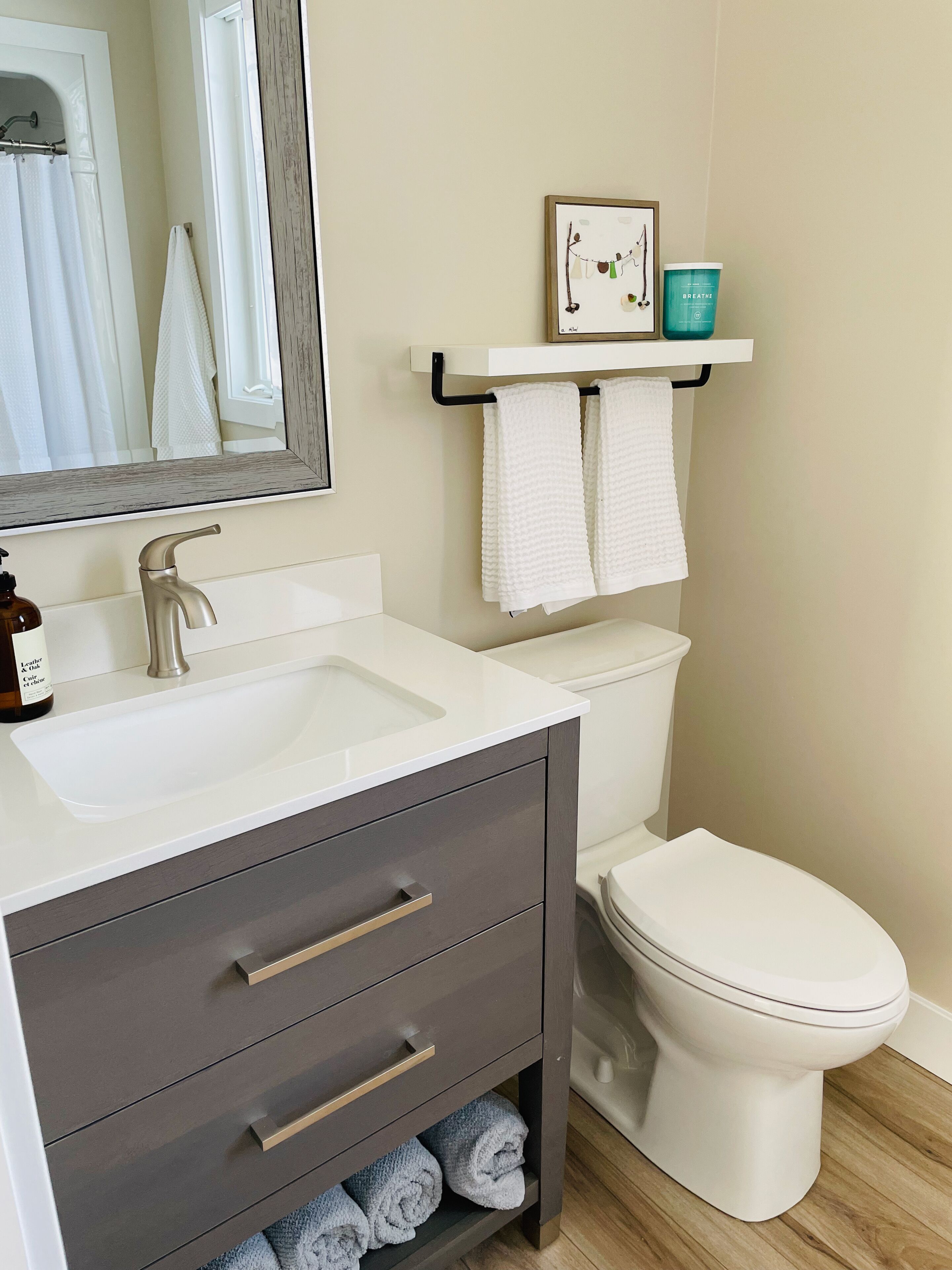 Une salle de bain avec un lavabo blanc, des tiroirs sombres, des toilettes et une étagère avec des serviettes et un tableau encadré.