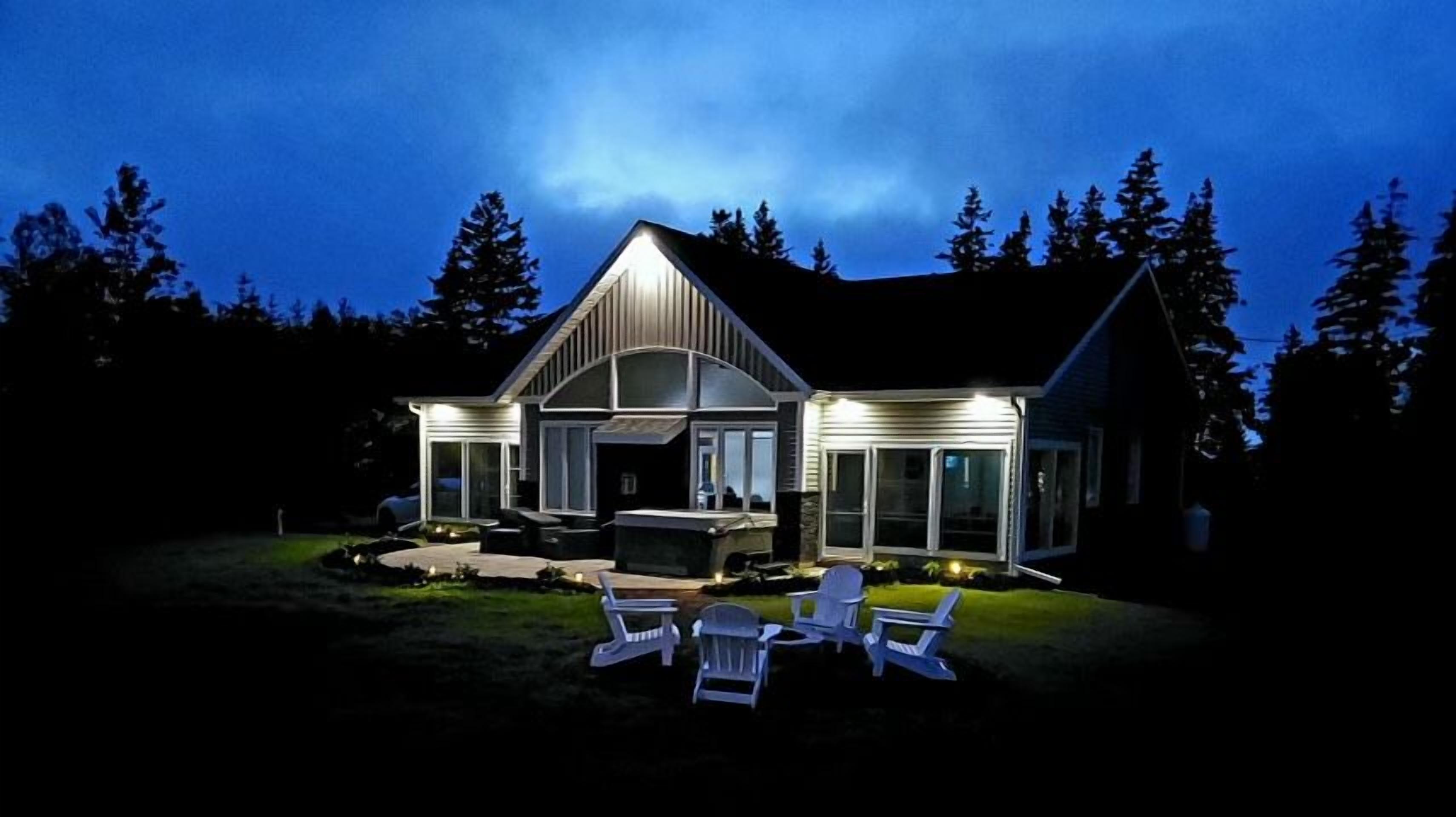 Una casa moderna con un porche cubierto, mobiliario exterior y un exterior bien iluminado durante la noche.