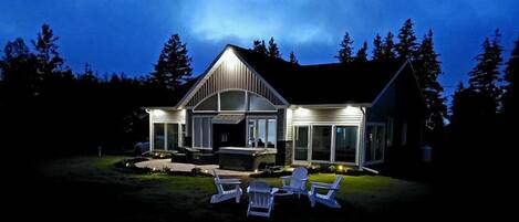 Una casa moderna con un porche cubierto, mobiliario exterior y un exterior bien iluminado durante la noche.