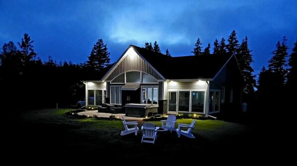 A modern house with a covered porch, outdoor seating, and a well-lit exterior at night.