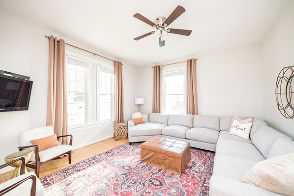 A living room with a sofa, ottoman, armchair, and a television.