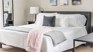 A neatly made bed with a fluffy pink throw, a bedside lamp, and three abstract paintings on the wall.