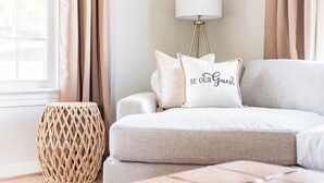 A cozy living room with a sofa, a round woven side table, and a lamp.