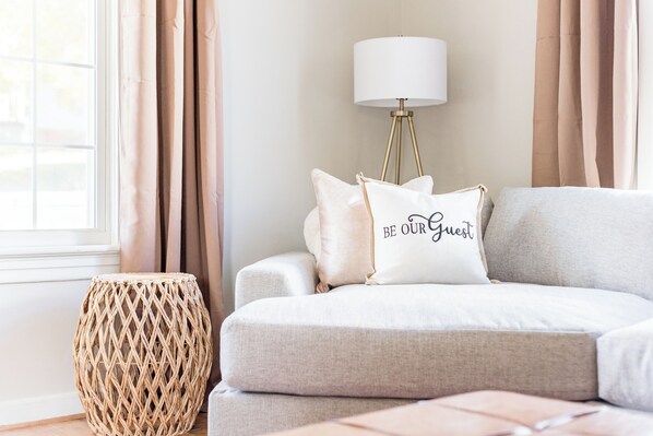 A cozy living room with a sofa, a round woven side table, and a lamp.