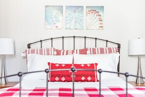 A bed with a metal frame, white and red bedding, and two wall-mounted lamps.