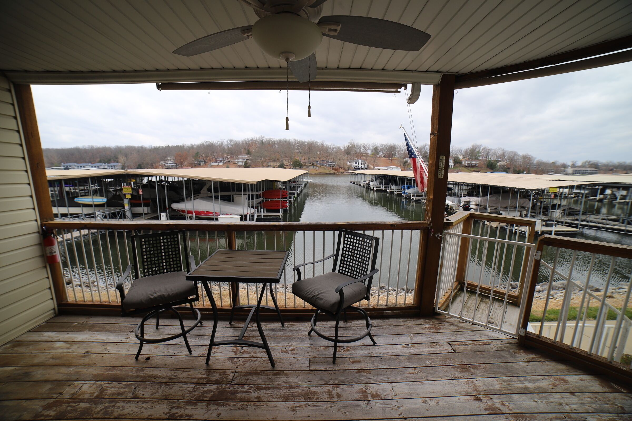 A covered outdoor area with a table and two chairs, overlooking a marina with boats and docks.