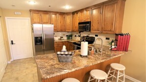 A kitchen with wooden cabinets, a stainless steel refrigerator, a microwave, a sink, and two bar stools. - 2 bed King Master/2 bath condo with lake access and large 16 x 40 boat slip (Osage Beach)